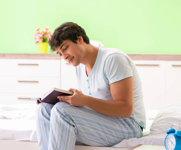 Young handsome student reading book in the bed - Foto, Imagen