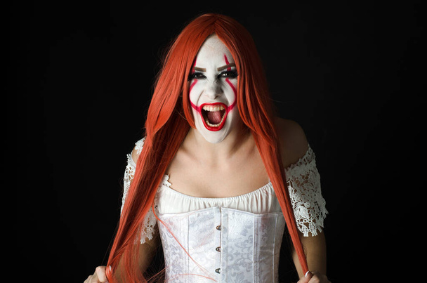 une fille en costume de clown avec un maquillage effrayant sur un fond noir
 - Photo, image