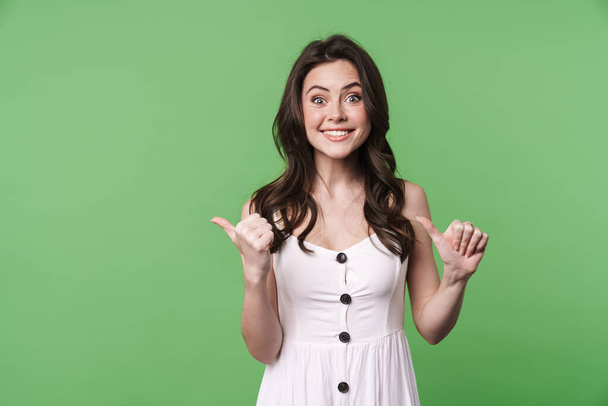 Image of joyful brunette woman smiling and pointing fingers aside isolated over green background - Fotó, kép