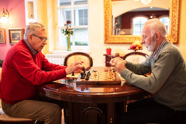 Two old friends playing a game of chess while sitting at the table - Фото, изображение