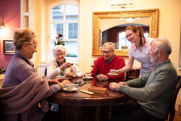 Nurse serving tea while older people play board games, retirement home - Фото, зображення