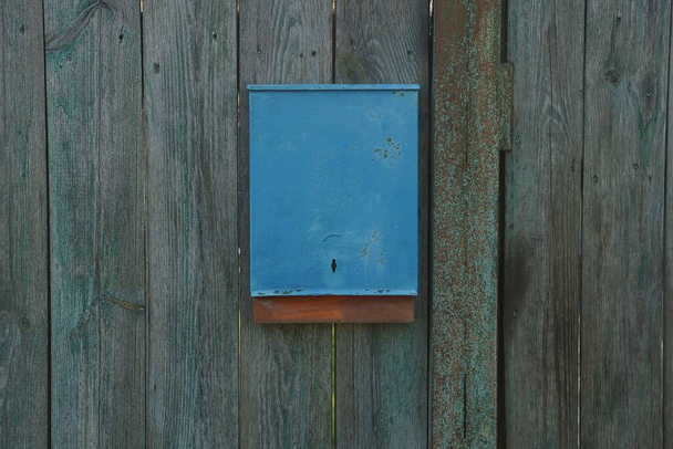 jedna niebieska metalowa skrzynka na listy wisząca na szarych drewnianych deskach ściany ogrodzenia - Zdjęcie, obraz