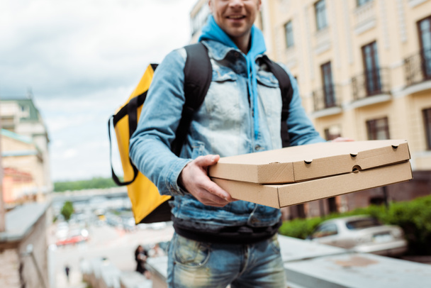 Vista recortada del repartidor sonriente sosteniendo cajas de pizza de cartón en la calle urbana
  - Foto, imagen