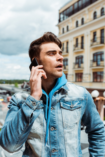 Красивий чоловік в джинсовій куртці говорить на смартфоні на міській вулиці
  - Фото, зображення