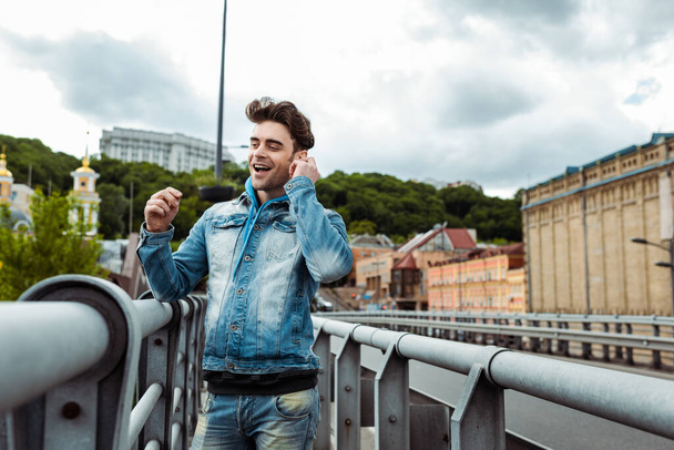 Selective focus of smiling man using earphones on urban street  - Foto, afbeelding