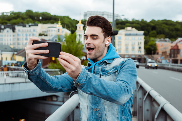 Ύπαρχος νεαρός άνδρας σε ακουστικά που τραβούσε φωτογραφίες με smartphone στη γέφυρα  - Φωτογραφία, εικόνα