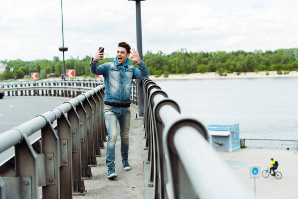 Focus selettivo dell'uomo allegro che fa videochiamate sullo smartphone mentre cammina sul ponte
  - Foto, immagini
