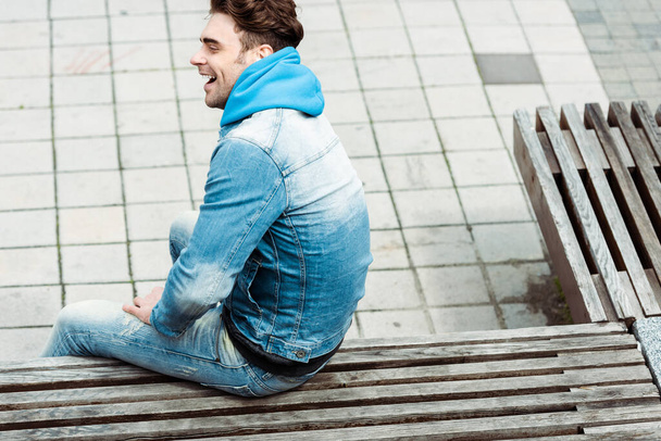 High angle view of positive man sitting on wooden bench on urban street  - Valokuva, kuva