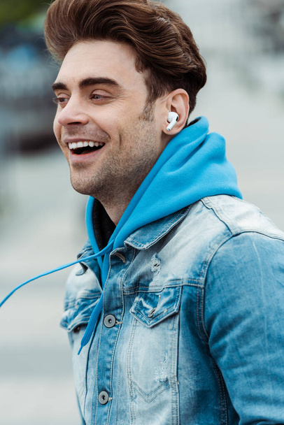 Χαμογελώντας άνθρωπος σε ακουστικά κοιτάζοντας μακριά σε εξωτερικούς χώρους  - Φωτογραφία, εικόνα