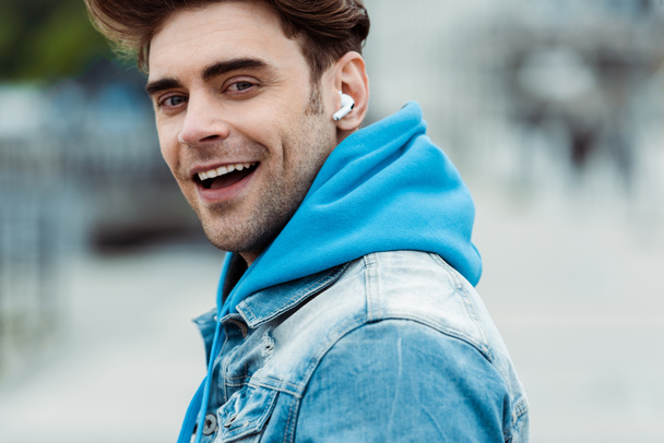 Πλευρική άποψη του όμορφος άντρας σε ακουστικά χαμογελώντας στην κάμερα σε εξωτερικούς χώρους  - Φωτογραφία, εικόνα