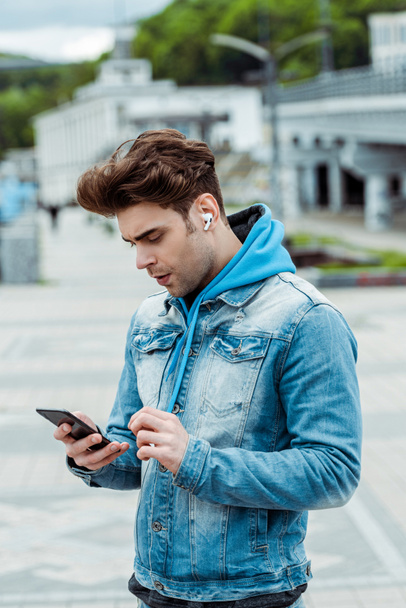 Jeune homme dans les écouteurs en utilisant smartphone sur la rue urbaine
  - Photo, image