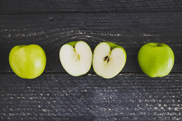 healthy plant-based food ingredients concept, green apples ined up on wooden table with some cut in half - Photo, image