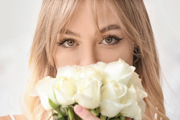 Schöne junge Frau mit einem Strauß Rosen auf hellem Hintergrund - Foto, Bild
