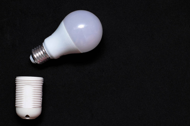 LED bulb and cartridge for it on a black background. Electricity Saving Concept. Place for text, copy space. - Foto, immagini