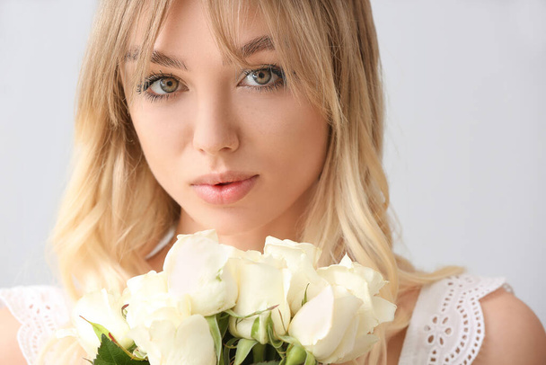 Beautiful young woman with bouquet of roses on light background - Фото, зображення