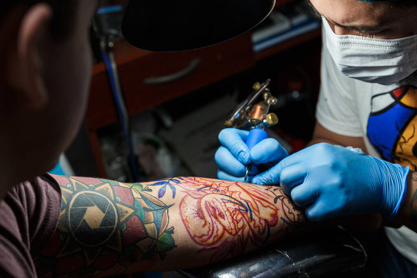 tetováló az ő gép tetoválás a karon a design húzott és használata védő maszk ellen covid 19, koncepció a művészet és design - Fotó, kép