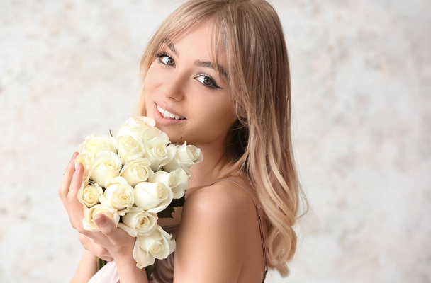 Όμορφη νεαρή γυναίκα με μπουκέτο τριαντάφυλλα στο φως φόντο - Φωτογραφία, εικόνα