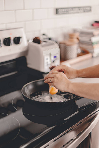 Breakfast preparation. Making morning meal. Weekday routine. Cooking food before work for family. Cracking the eggs into the pan. Home lifestyle. Brunch with husband. Stove, toaster. Selective focus - Foto, Imagen