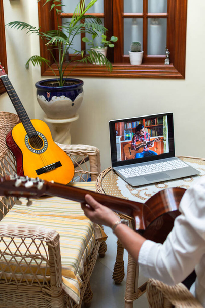 Femme apprenant à jouer de la guitare avec une classe à distance ou un tutoriel à l'aide d'un ordinateur dans une belle pièce de la maison pleine de plantes. Technologie et apprentissage à domicile
. - Photo, image
