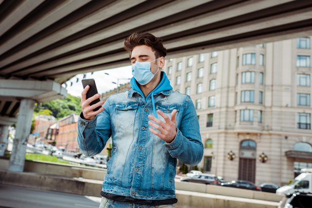 Man in medical mask holding cellphone on city street  - Foto, Bild