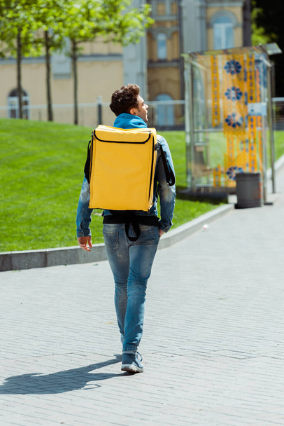 Vista trasera del mensajero con mochila termo caminando por la calle urbana
  - Foto, Imagen