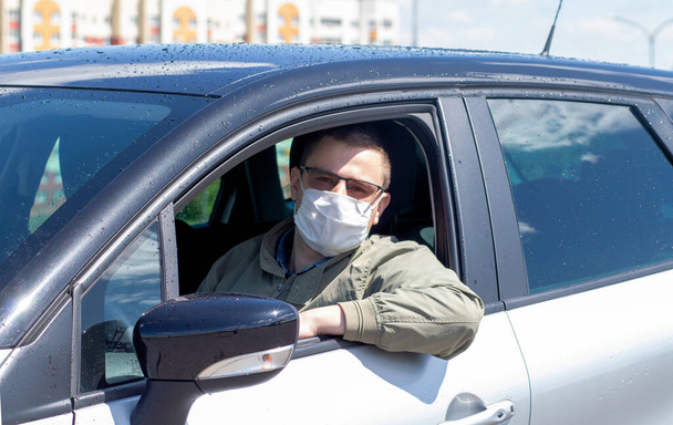Protect yourself from the coronavirus with a mask while driving. A masked driver in a silver car - Photo, Image