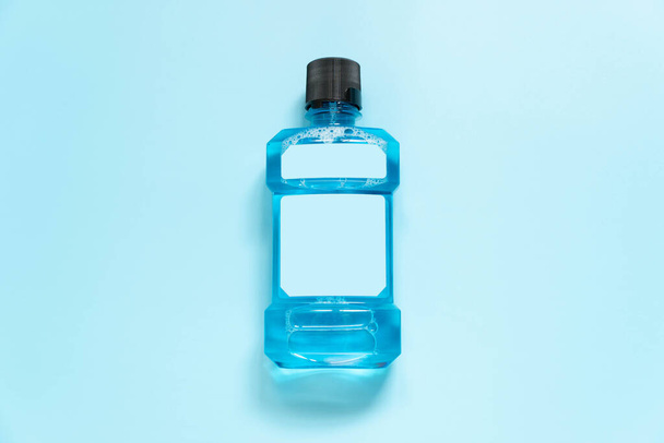 Açık mavi arka planda ağız temizliği için boş etiketli gargara şişesi. Ağız durulama sıvıları kötü nefeslere, çürüklere ve plaklara iyi gelir. Diş bakımı ürünü. Üst görünüm. - Fotoğraf, Görsel