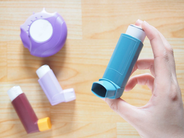 Ręce pacjenta trzymające niebieski inhalator astmy z zestawem inhalatorów astmy / POChP na drewnianym stole. Produkty farmaceutyczne stosowane w leczeniu zapalenia płuc i ataku astmy. Zdrowie i koncepcja medyczna. - Zdjęcie, obraz