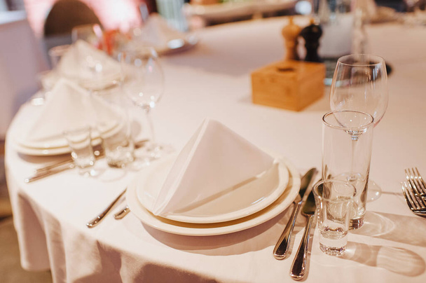 Ravintola, juhla-ateria, kattaus. Pöytä on peitetty valkoisella pöytäliinalla, astioilla, valkoisilla puhtailla lautasilla, ruokailuvälineillä, lautasliinoilla, viinilaseilla, kynttilöillä. lähikuva. - Valokuva, kuva