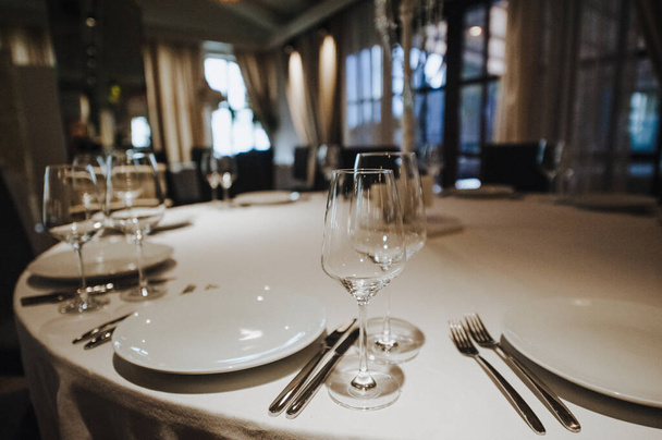 Restaurante, banquete, mesa. La mesa está cubierta con un mantel blanco, platos, platos blancos limpios, cubiertos, servilletas, copas de vino, velas. Primer plano
. - Foto, Imagen