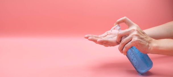 Woman hands using wash hand sanitizer gel pump dispenser. Clear sanitizer in pump bottle, for killing germs, bacteria and virus, pink background - Foto, afbeelding