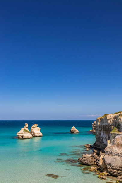 Die Bucht von Torre dell 'Orso mit ihren hohen Klippen in Salento, Apulien, Italien. Türkisfarbenes Meer und blauer Himmel, sonniger Sommertag. Die Stapel genannt die zwei Schwestern, eingetaucht in das Meer. - Foto, Bild