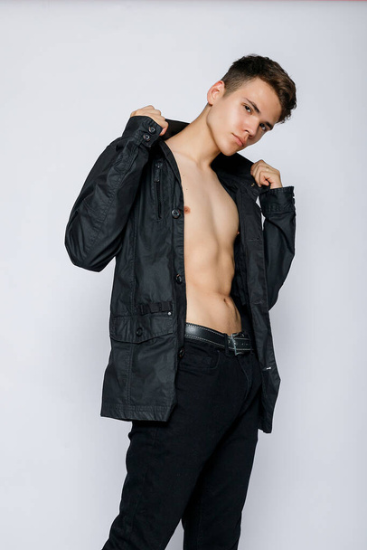 Young muscular man in a black jacket and jeans. young handsome man, leather jacked on naked torso, emotional posing, white background, modern guy, lifestyle people concept - Photo, image