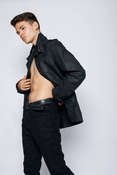 Young muscular man in a black jacket and jeans. young handsome man, leather jacked on naked torso, emotional posing, white background, modern guy, lifestyle people concept - Photo, Image
