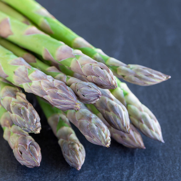 Bunch of fresh green asparagus on  dark slate background, square format - Фото, изображение