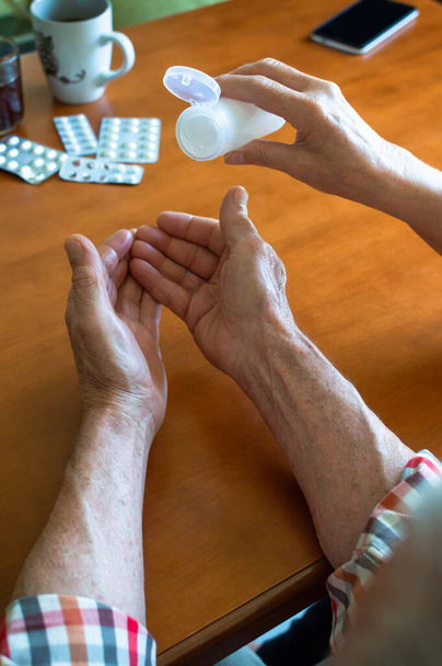 Terveys vanhuksille: vanhempi pari, joka käyttää käsinpuhdistusgeeliä ja järjestää lääkkeitä kotona. Suoja infektioita ja kovia tauteja vastaan 19. - Valokuva, kuva