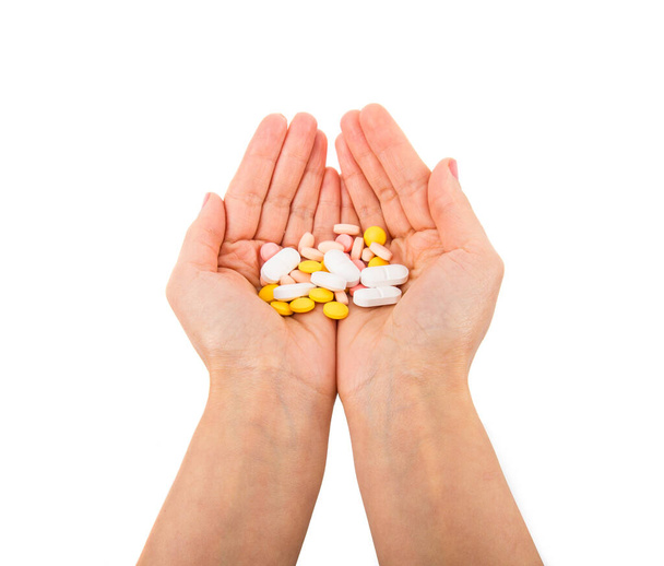 Kéz egy maroknyi szétszórt gyógyszerek, tabletták és tabletták fehér alapon. - Fotó, kép