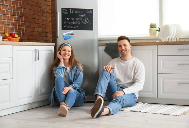 Happy couple sitting on floor near refrigerator in kitchen - Photo, Image