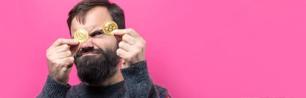 A pensive guy with a beard against a pink background. Thinking about question, pensive expression, looks incredulous. Change in the growth and fall of cryptocurrency. - Foto, afbeelding