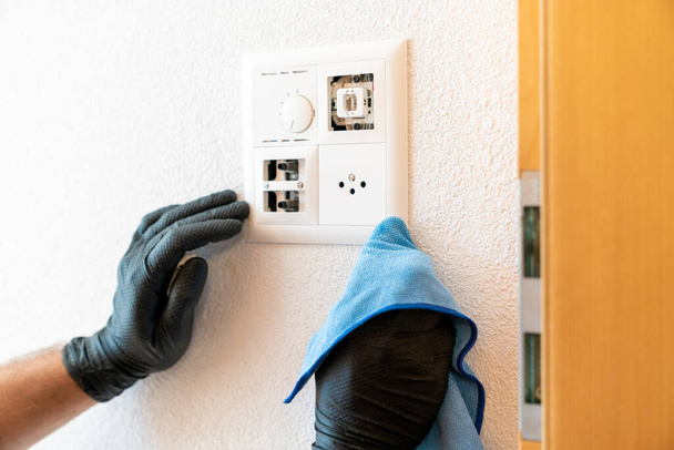 A close up of a professional cleaner cleaning a modern light switch and dimmer and socket with a micro fiber cloth - Foto, imagen