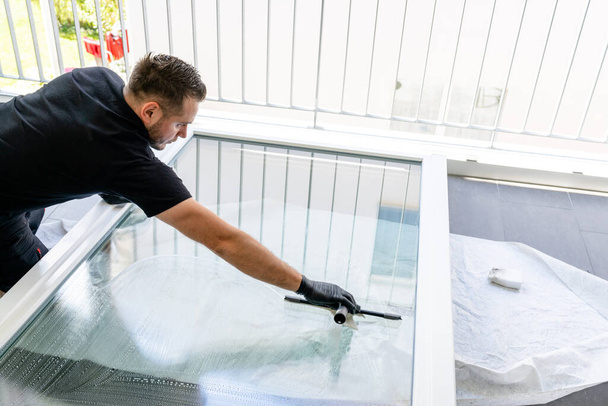 Un nettoyeur de vitres professionnel utilisant une raclette de nettoyage de vitres pour nettoyer une grande fenêtre pliante de l'appartement
 - Photo, image