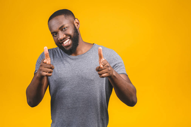 Portrait of cheerful, positive, handsome man with black skin, beaming smile in casual showing thumb up with finger to the camera isolated on yellow background. - Zdjęcie, obraz