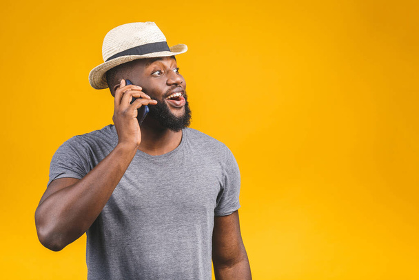 Portrait of a happy travel african american guy talking on mobile phone isolated against yellow background.  - Фото, изображение