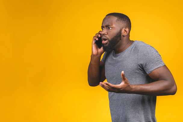 Hombre afroamericano joven usando teléfono inteligente estresado, sorprendido con la vergüenza y la cara sorpresa, enojado y frustrado. Miedo y malestar por error
.  - Foto, Imagen