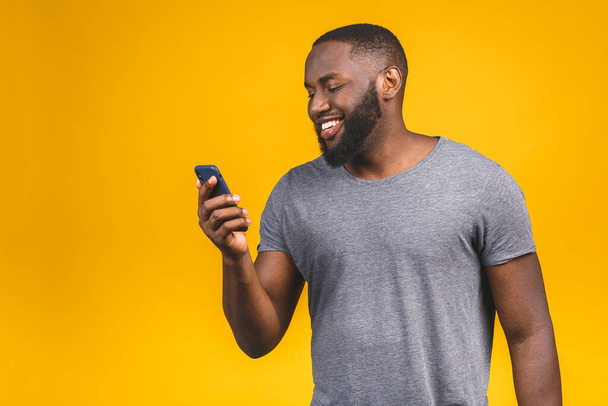 Portrait of handsome excited cheerful joyful delightful curious guy wearing casual sending and getting messages to his lover isolated against yellow background. Using phone.  - Valokuva, kuva