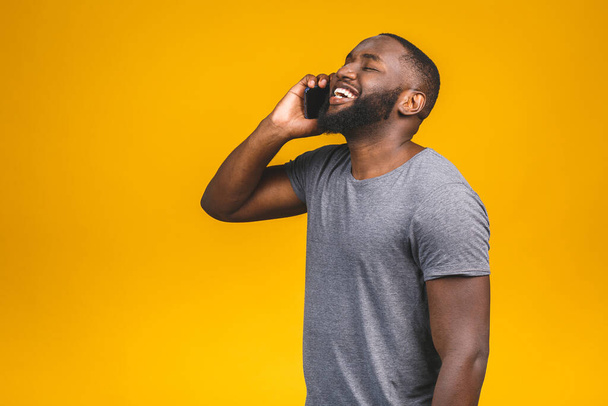 Portret van een gelukkige Afro-Amerikaanse man praten op mobiele telefoon geïsoleerd tegen een gele achtergrond.  - Foto, afbeelding
