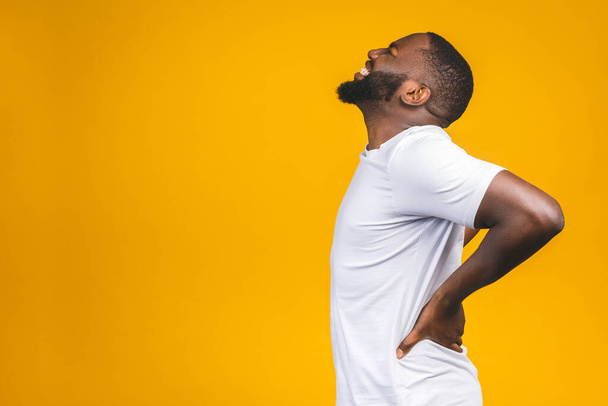 Junger afroamerikanischer junger Mann leidet unter Rückenschmerzen, weil er sich um isolierten Hintergrund bemüht hat. - Foto, Bild