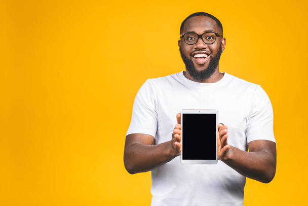 Risate giovane afroamericano in possesso di un touch pad tablet PC su isolato su sfondo giallo. - Foto, immagini