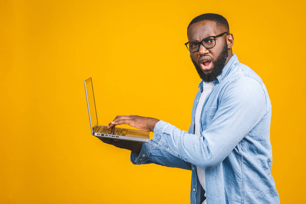 afroamericano ypung uomo spaventato una cattiva notizia sul suo computer portatile, isolato su sfondo giallo.  - Foto, immagini