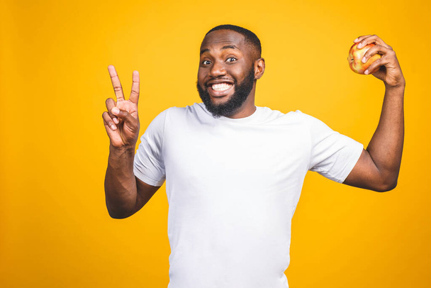 Healthy african american man holding an apple isolated against yellow background.  - 写真・画像
